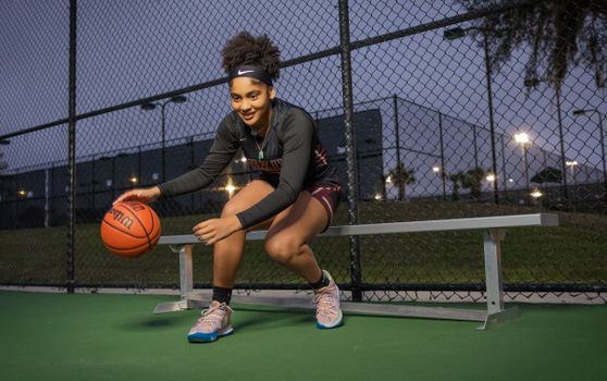 Energetic young woman playing basketball on outdoor court at night, showcasing athletic skill and fun.