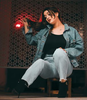 Stylish woman in denim outfit with tattoos, sitting confidently, capturing modern fashion trends.