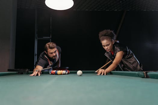 Two people focusing on a game of pool, aiming to make a shot with cue sticks on a billiard table.