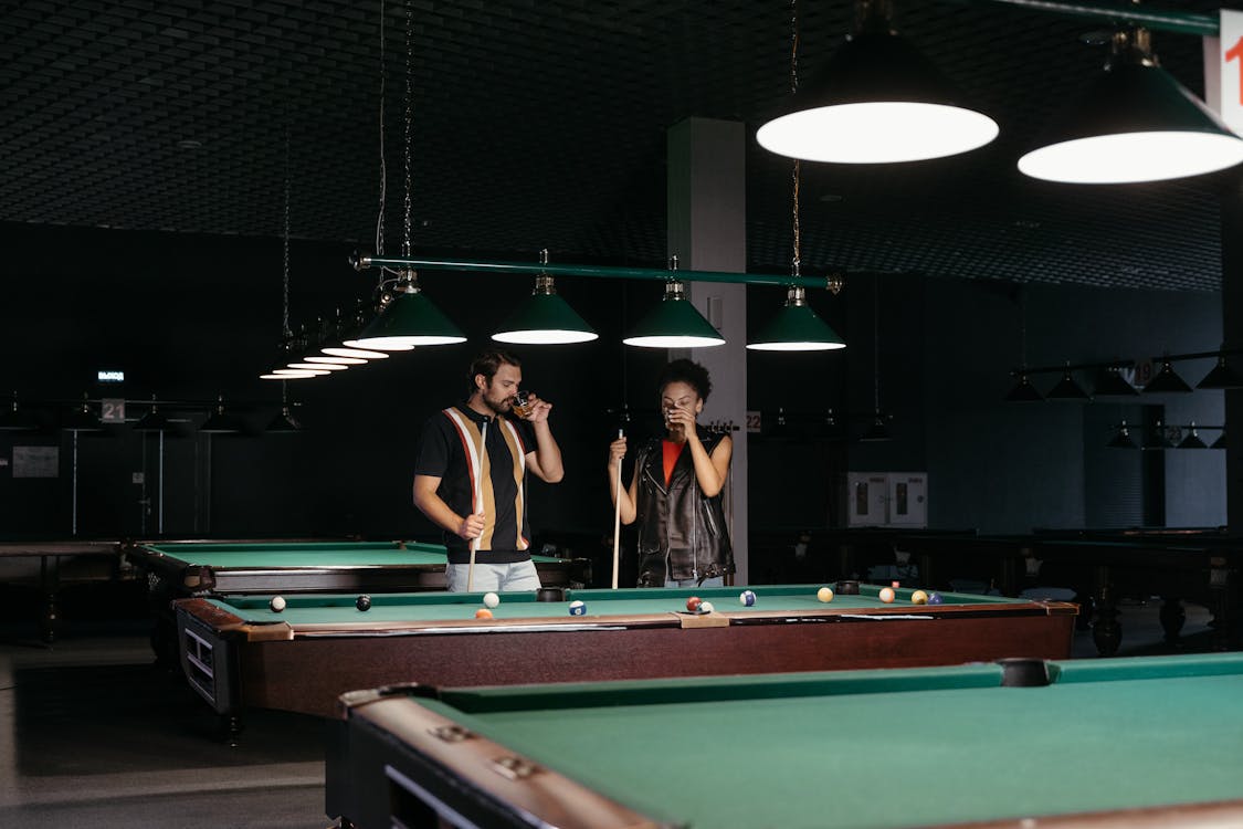 A Man and a Woman Drinking Alcoholic Beverage while Holding Cue Sticks