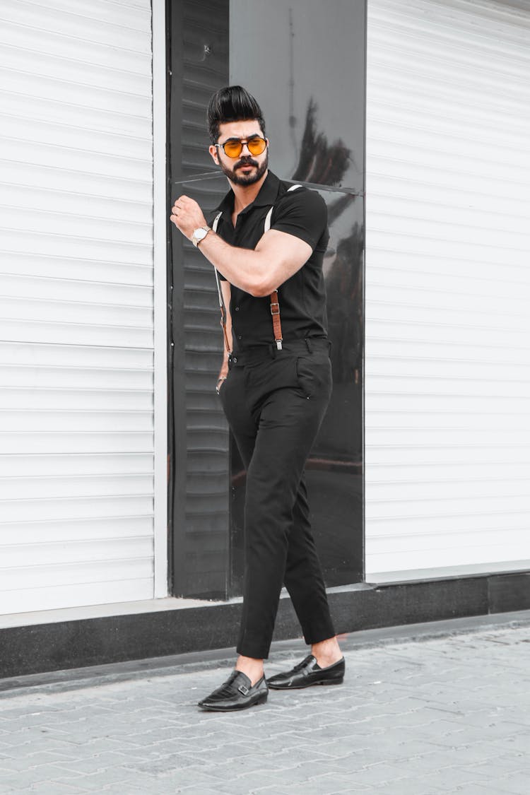 A Man In Black Button Up Polo And Black Pants Standing On Sidewalk 