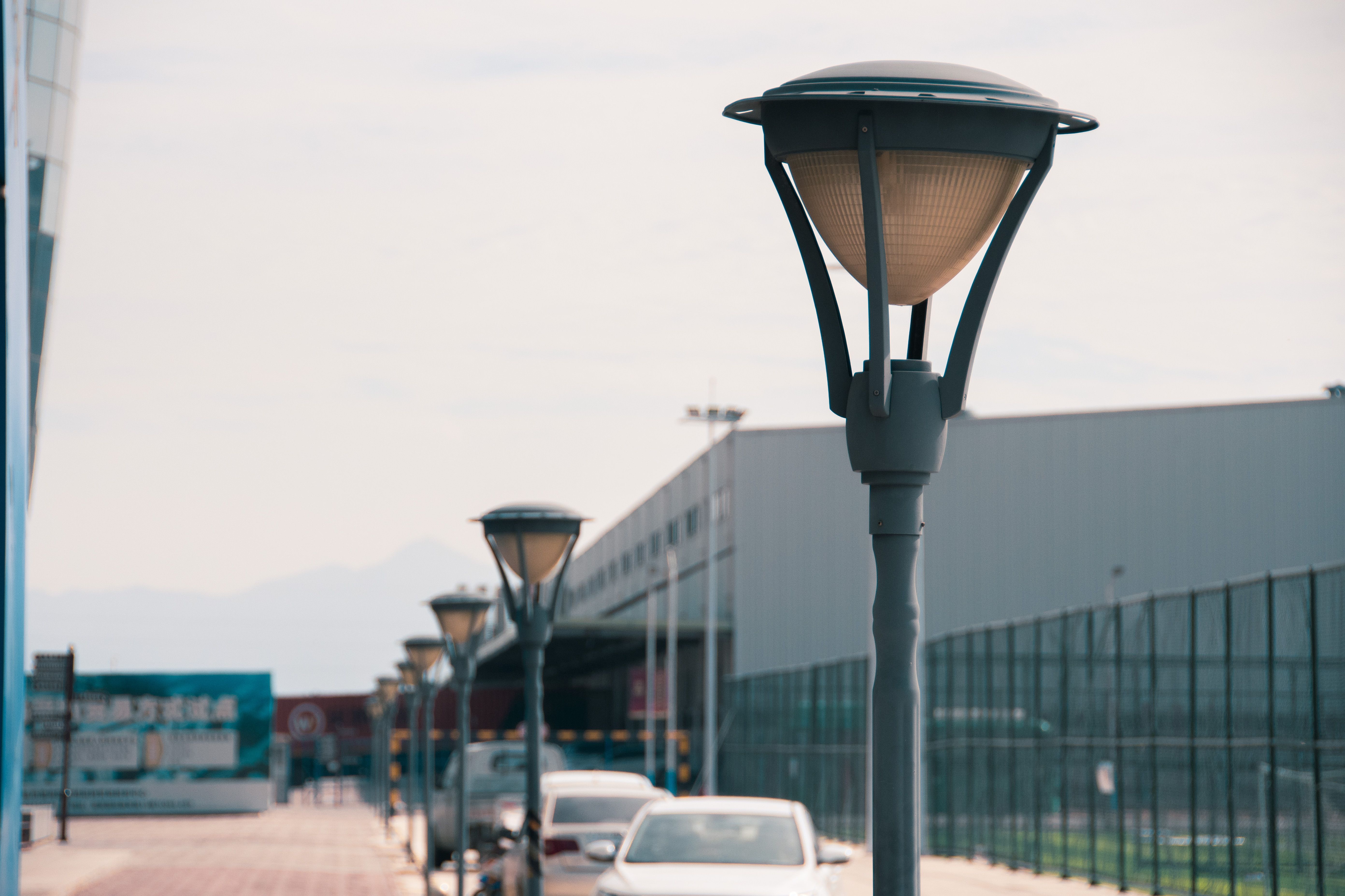 Close-up of street lamps with cars and buildings in an urban setting during daytime.