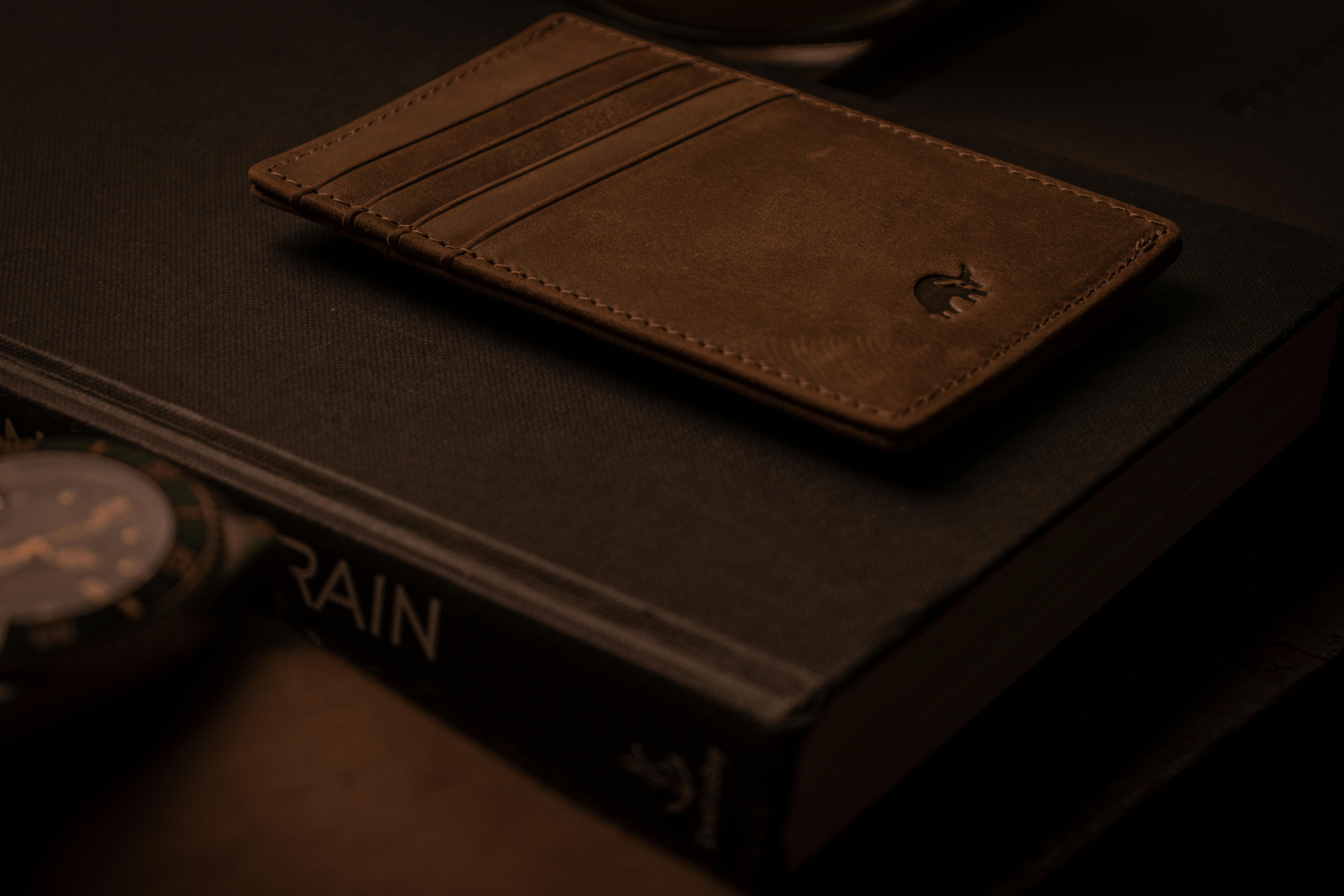 brown leather wallet on top of a book in close up photography