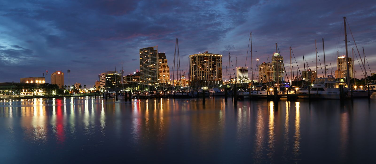 Scenic view of St. Petersburg, FL marina at dusk, featuring skyline and reflections in water.