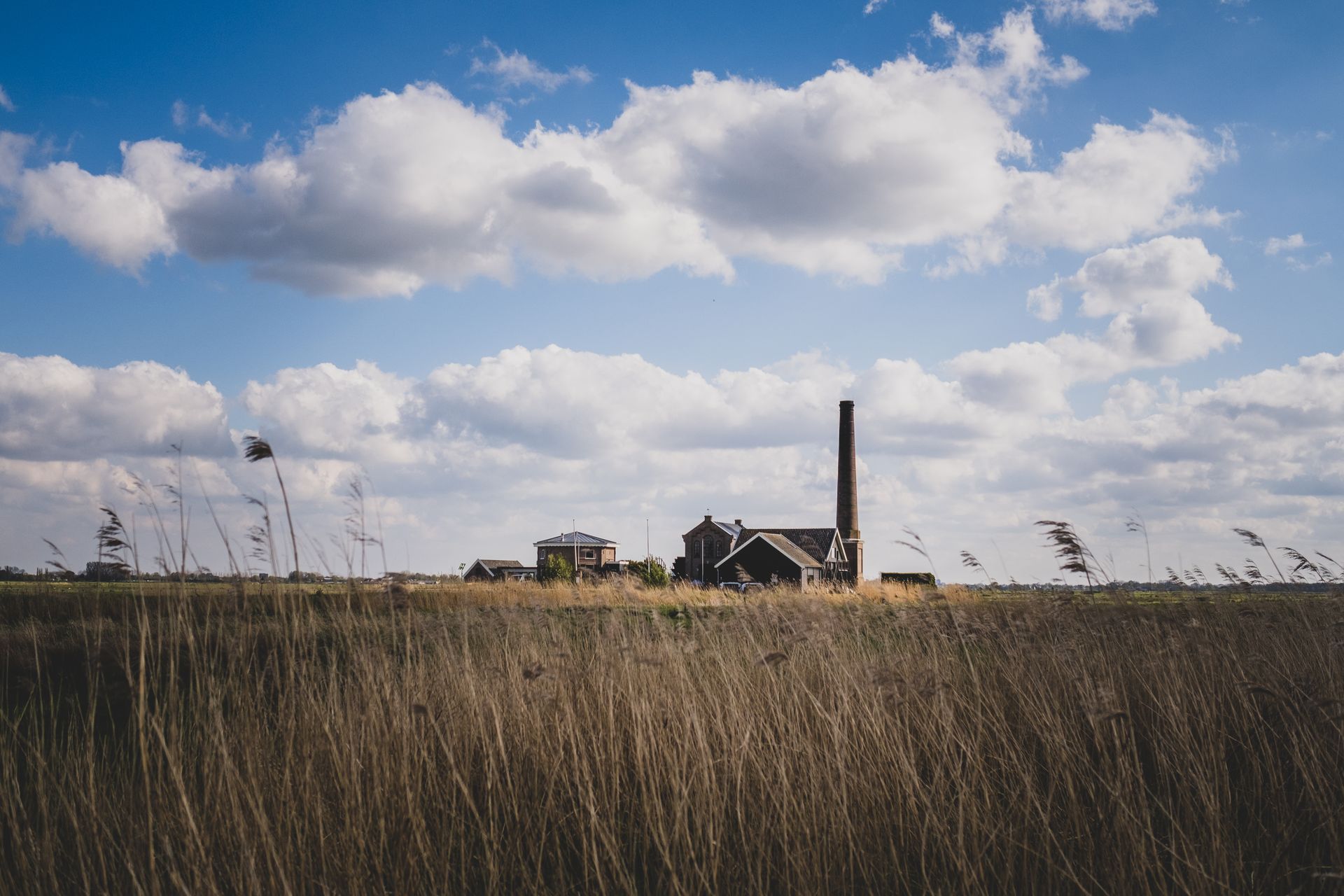 Scenic view of countryside farm buildings under a cloudy blue sky amidst a vast grass field.