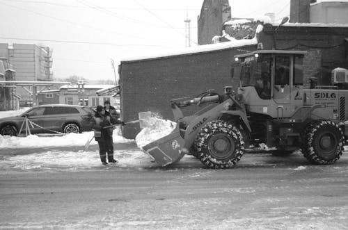 A Grayscale Photo of a Man Putting Snow on a Heavy Equipment