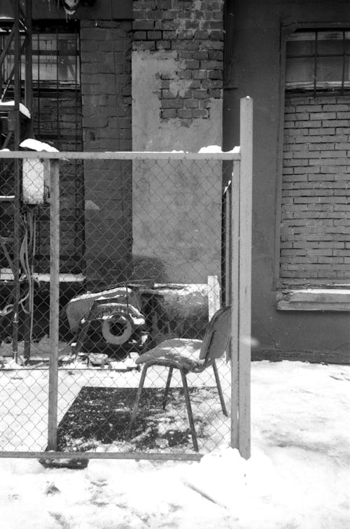 Grayscale Photo of Chair near the Chain Link Fence 