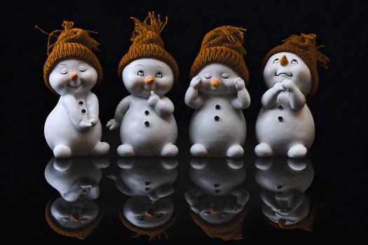 Four snowman figurines with beanies, showcasing expressions with a reflective surface.