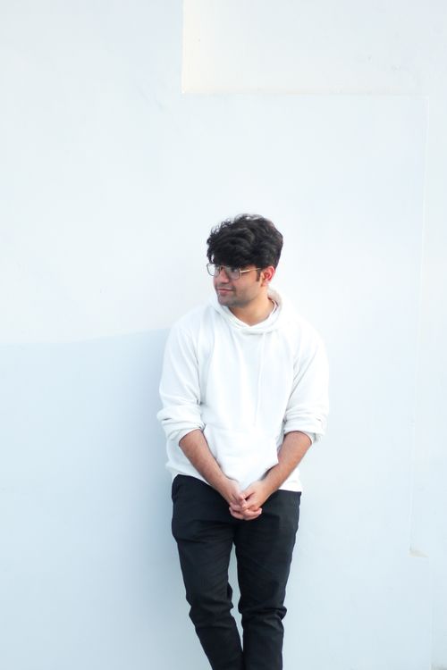 Free Casual young man in a white hoodie leaning against a white wall, looking thoughtful. Stock Photo