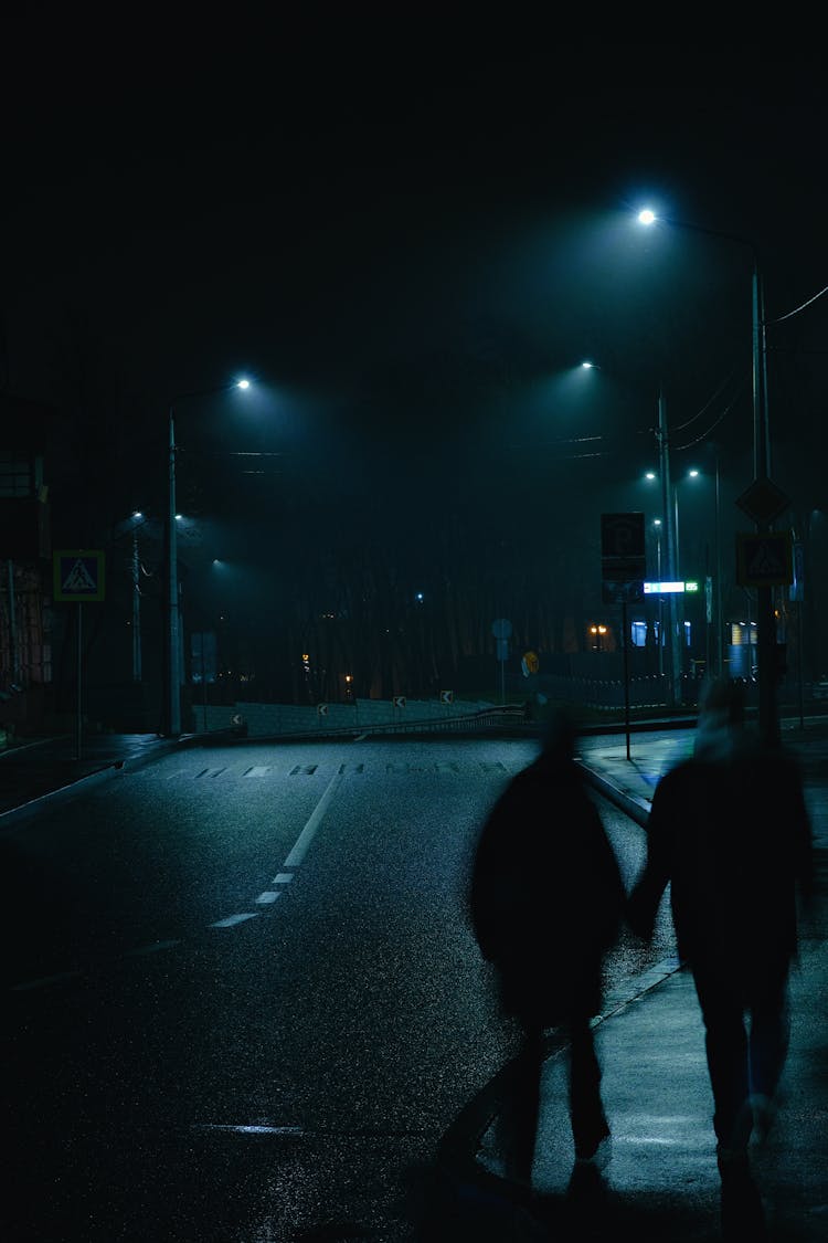 Silhouettes Of People Walking On Street At Night