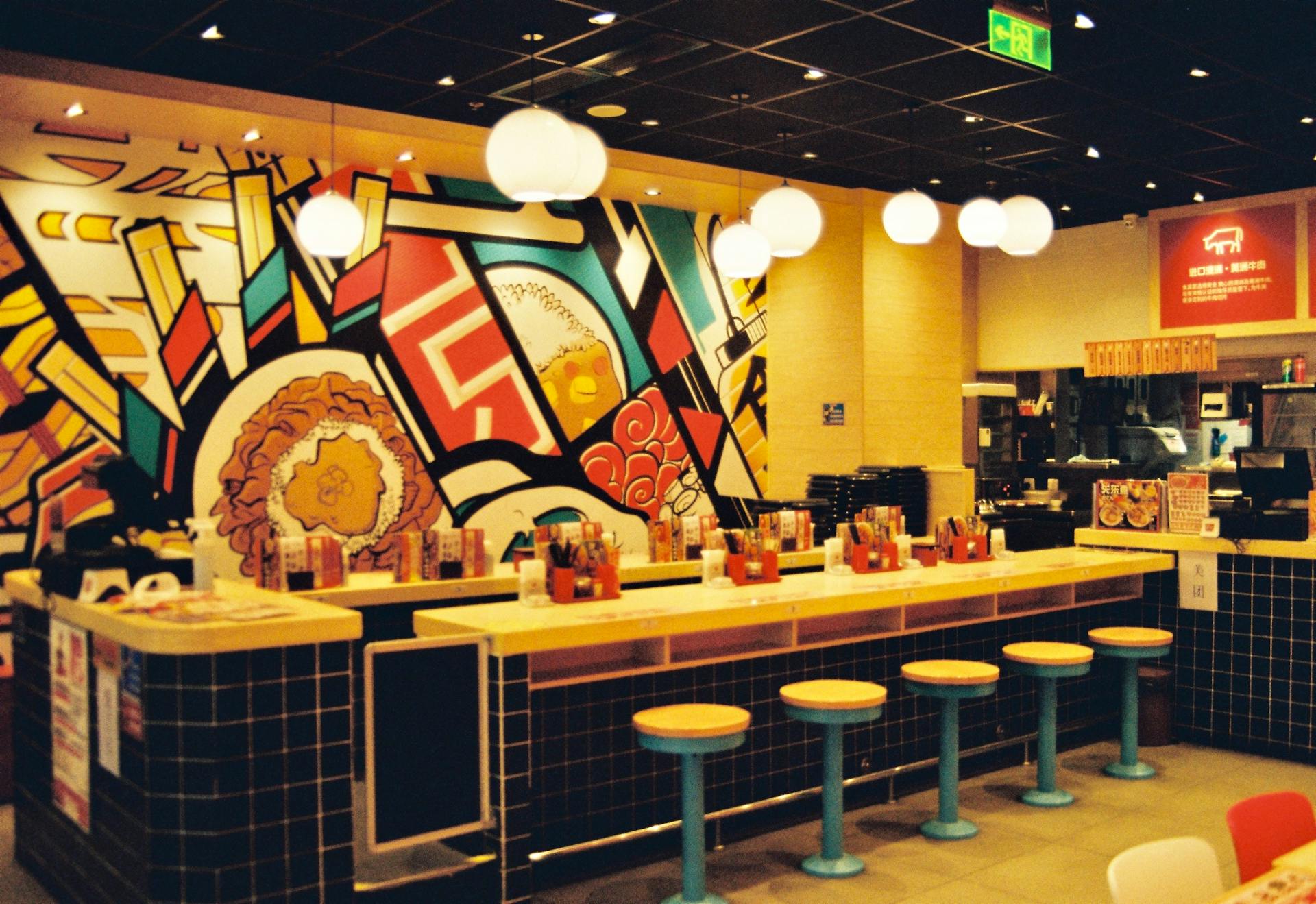 A colorful and modern fast food restaurant interior with artistic wall decor and hanging lights.