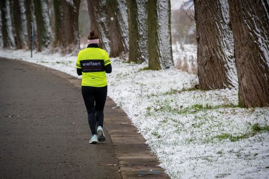 A woman walks down a snow-lined path in winter, wearing bright running gear.