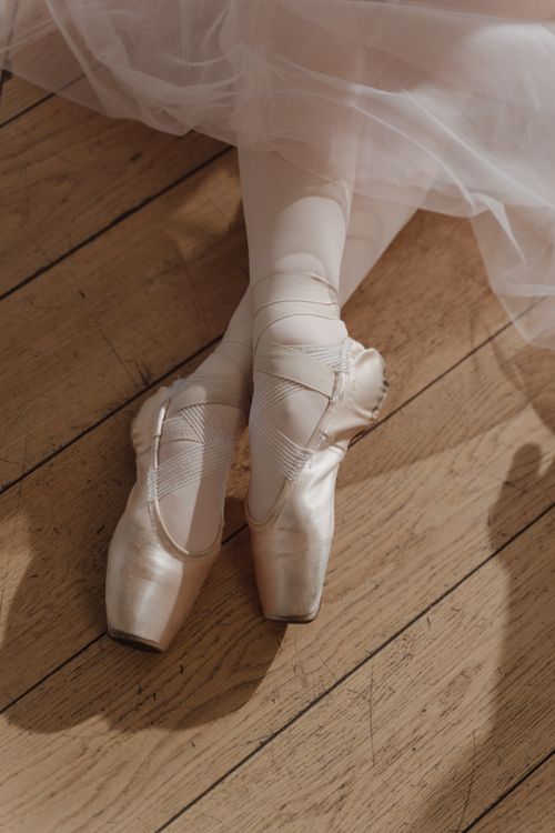 Free Close-up of pointe shoes and tutu on wooden flooring, capturing a serene ballet moment. Stock Photo