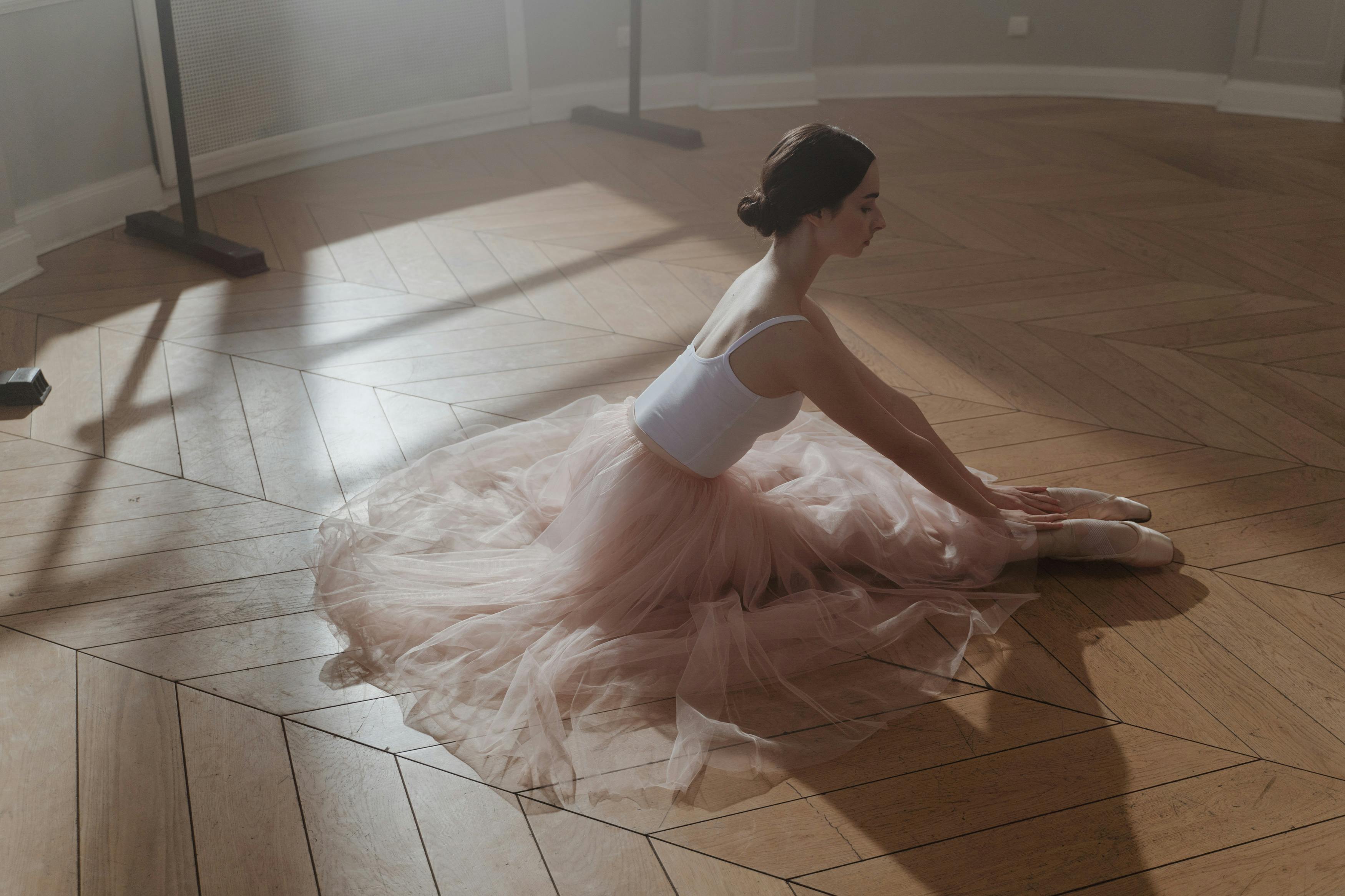 A serene ballerina in tulle tutu gracefully stretches on a wooden floor, bathed in warm light.