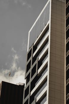 Low angle view of a modern high-rise building with glass panels and a cloudy sky backdrop.