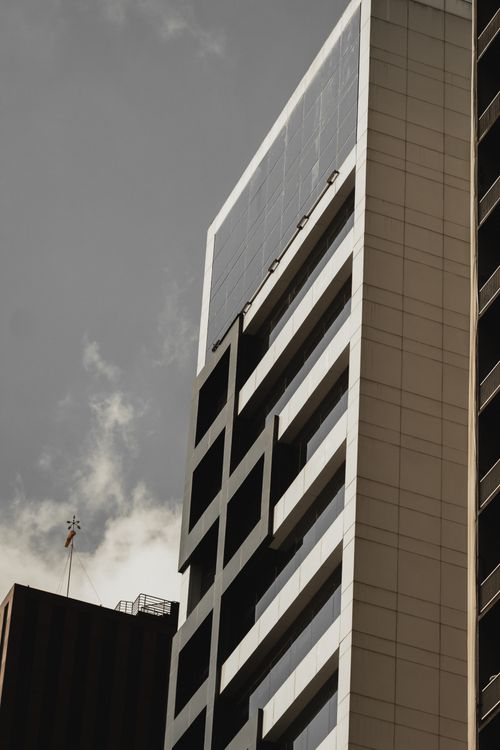 Free Low angle view of a modern high-rise building with glass panels and a cloudy sky backdrop. Stock Photo