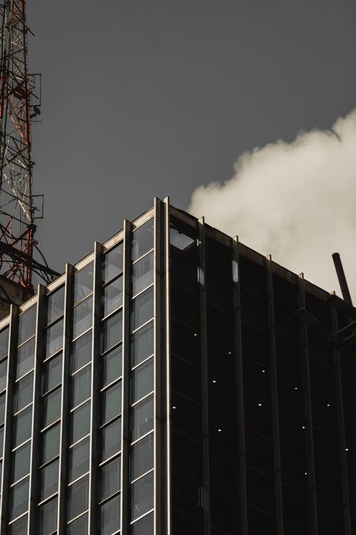 Free Close-up of a modern skyscraper with a tower, set against a cloudy sky, showcasing architectural design. Stock Photo