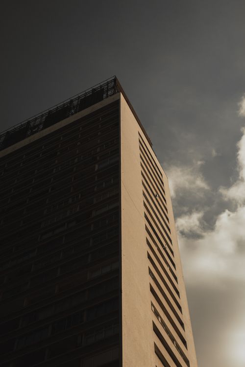 Free A low angle view of a skyscraper facade against a moody, cloudy sky, highlighting architectural design. Stock Photo