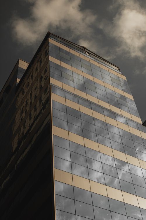 Free A modern glass skyscraper with a reflective facade under a moody sky. Stock Photo
