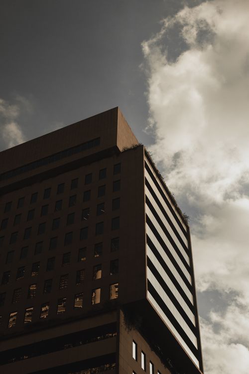 Free Low angle of a modern building against a dramatic cloudy sky, highlighting architectural design. Stock Photo