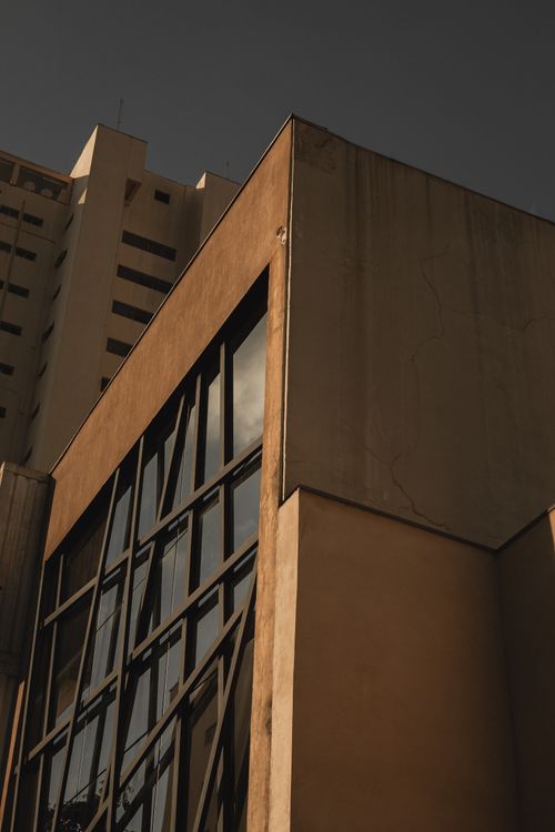 Free A low-angle view of a modern building featuring large reflective windows and concrete walls under a moody sky. Stock Photo