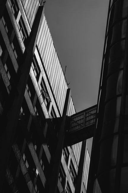 Fotomural Foto en blanco y negro de edificios modernos interconectados con una pasarela angular.