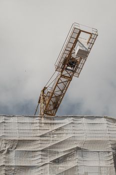Tower crane operates over a partially covered structure against a cloudy sky.