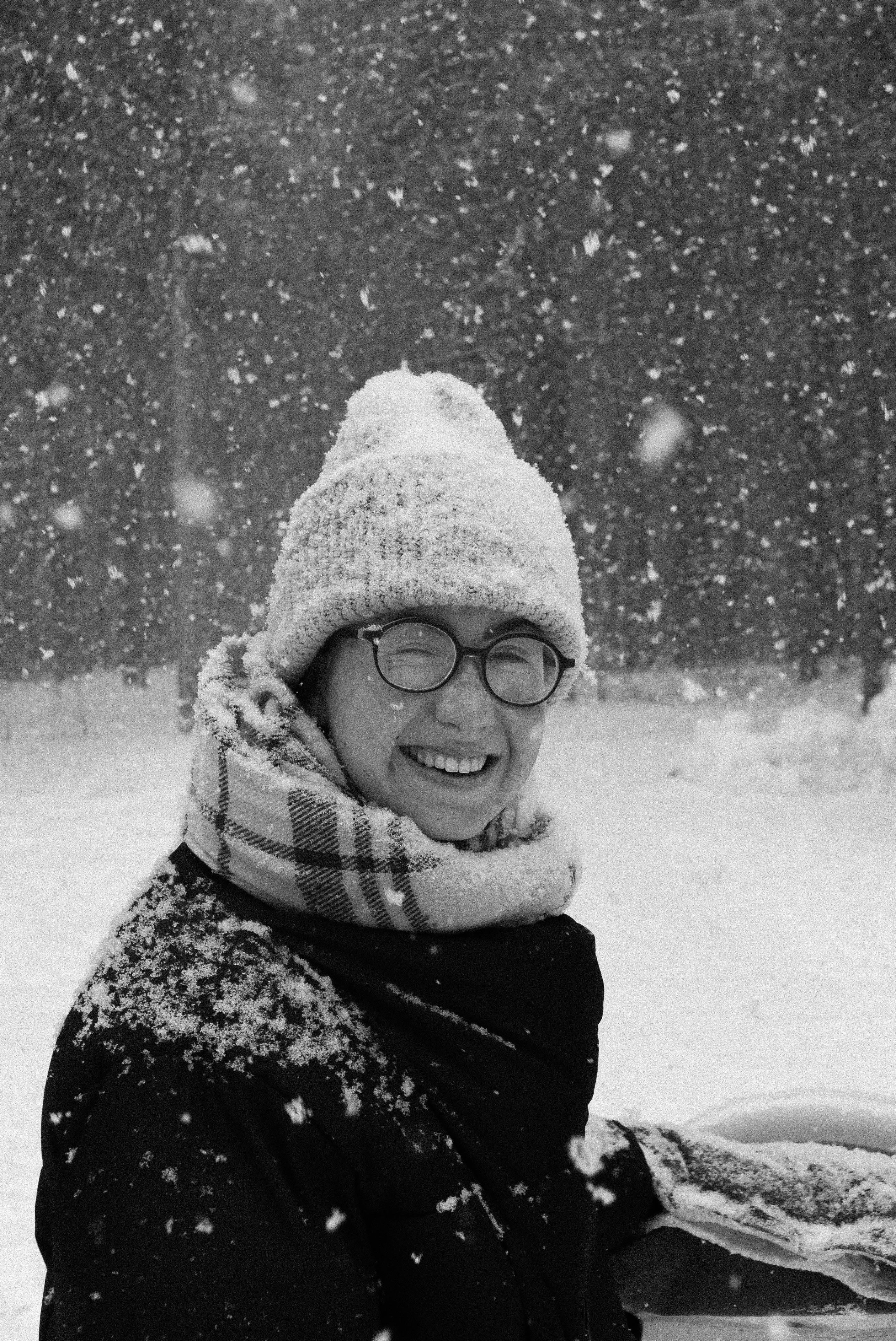 Woman wearing a beanie and eyeglasses, smiling in a snowy landscape.