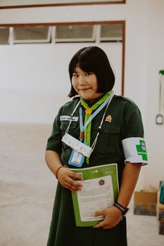 Young Asian girl in school uniform confidently holding a certificate, indoors.