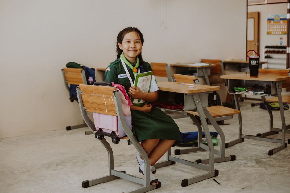 A young student smiles confidently while sitting in a classroom, embracing education.