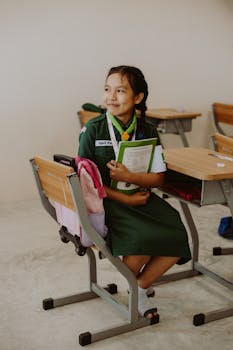 Young student in scout uniform, smiling in classroom while holding textbooks.