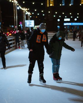 Couple enjoying a night ice skating under festive lights.