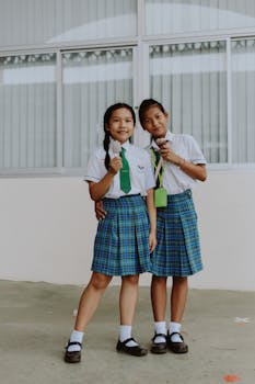 Two teenage girls in school uniforms enjoying ice cream together outdoors.