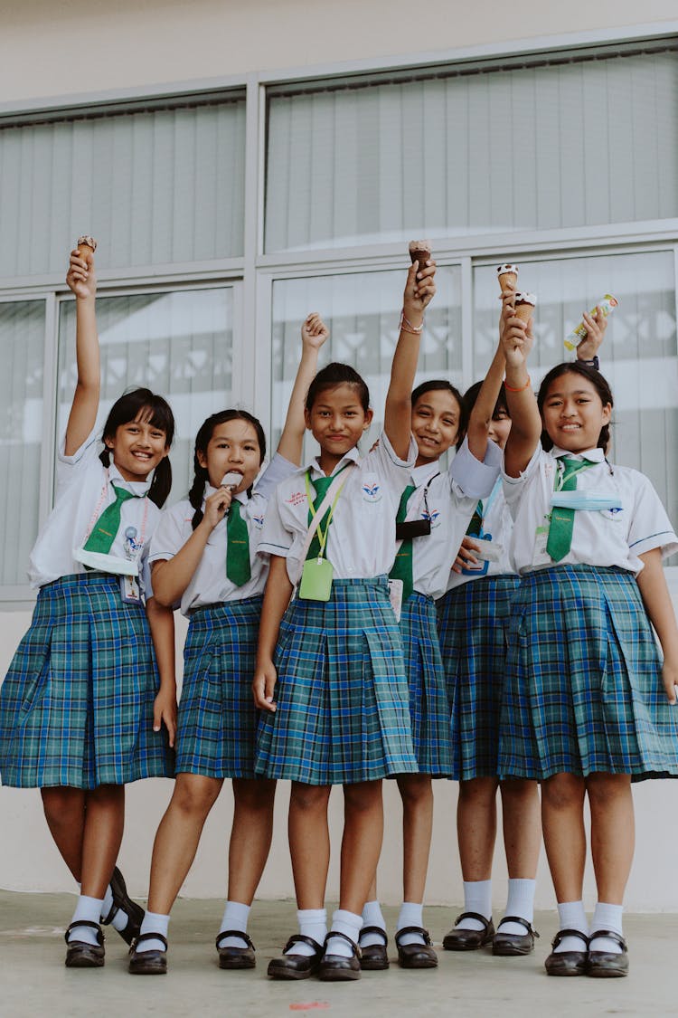 A Group Of Girls In School Uniform Standing While Raising Their Hands