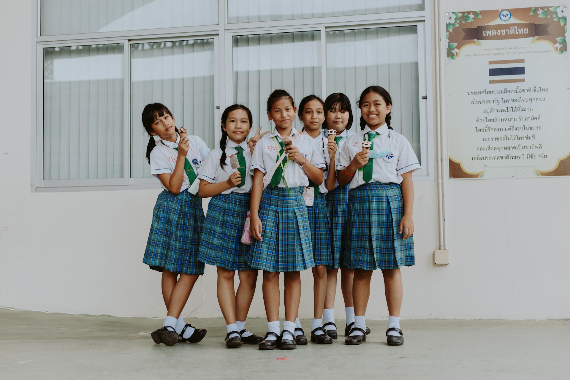 Six schoolgirls in uniform enjoying ice cream outside their school building in Thailand.