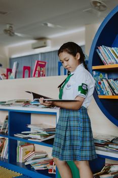 Young girl in school uniform engrossed in reading a book at a library.