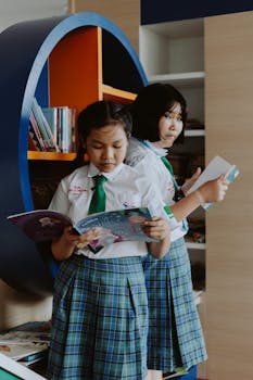 Two girls in school uniform reading books in a library setting.