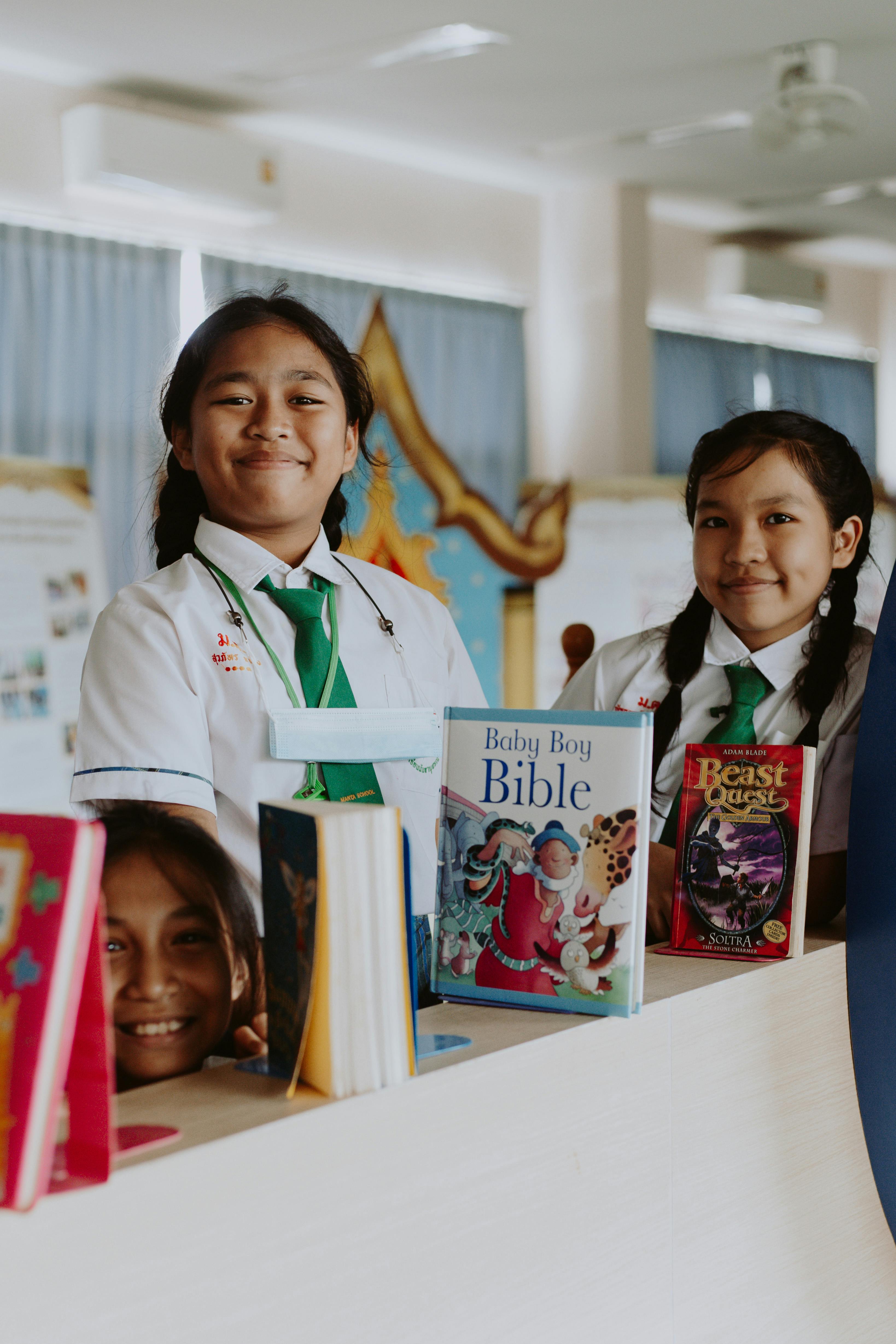 Free Group of Asian girls in school uniforms smiling by a library bookshelf with books displayed. Stock Photo