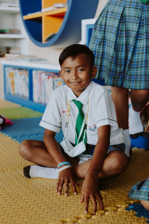 Portrait of Smiling Boy in School Uniform Sitting on Floor in Classroom