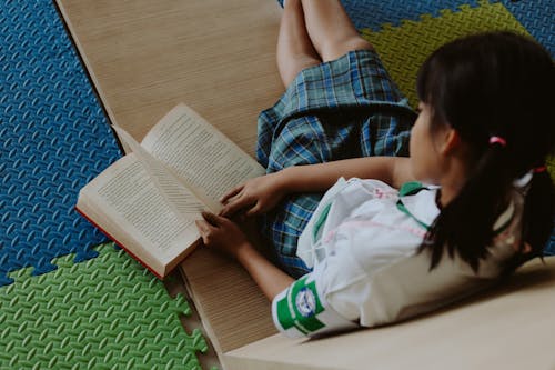 Free Girl in School Uniform Reading Book on Floor in Classroom Stock Photo