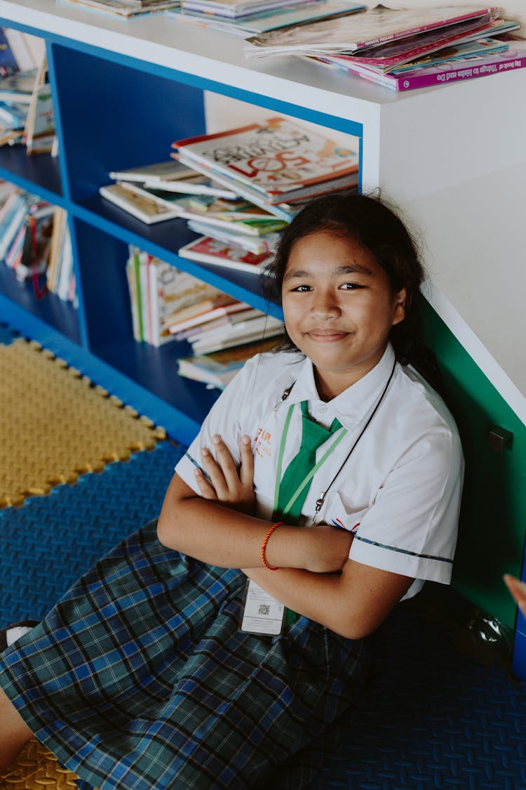 Portrait Of Smiling Girl In School Uniform Sitting On Floor With Arms Crossed