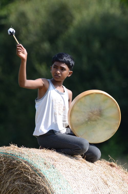 Free A child plays a drum while sitting on a hay bale in a sunny rural setting. Stock Photo
