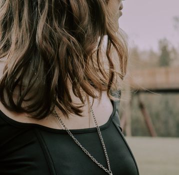 Close-up of a person with wavy hair wearing a necklace outdoors.
