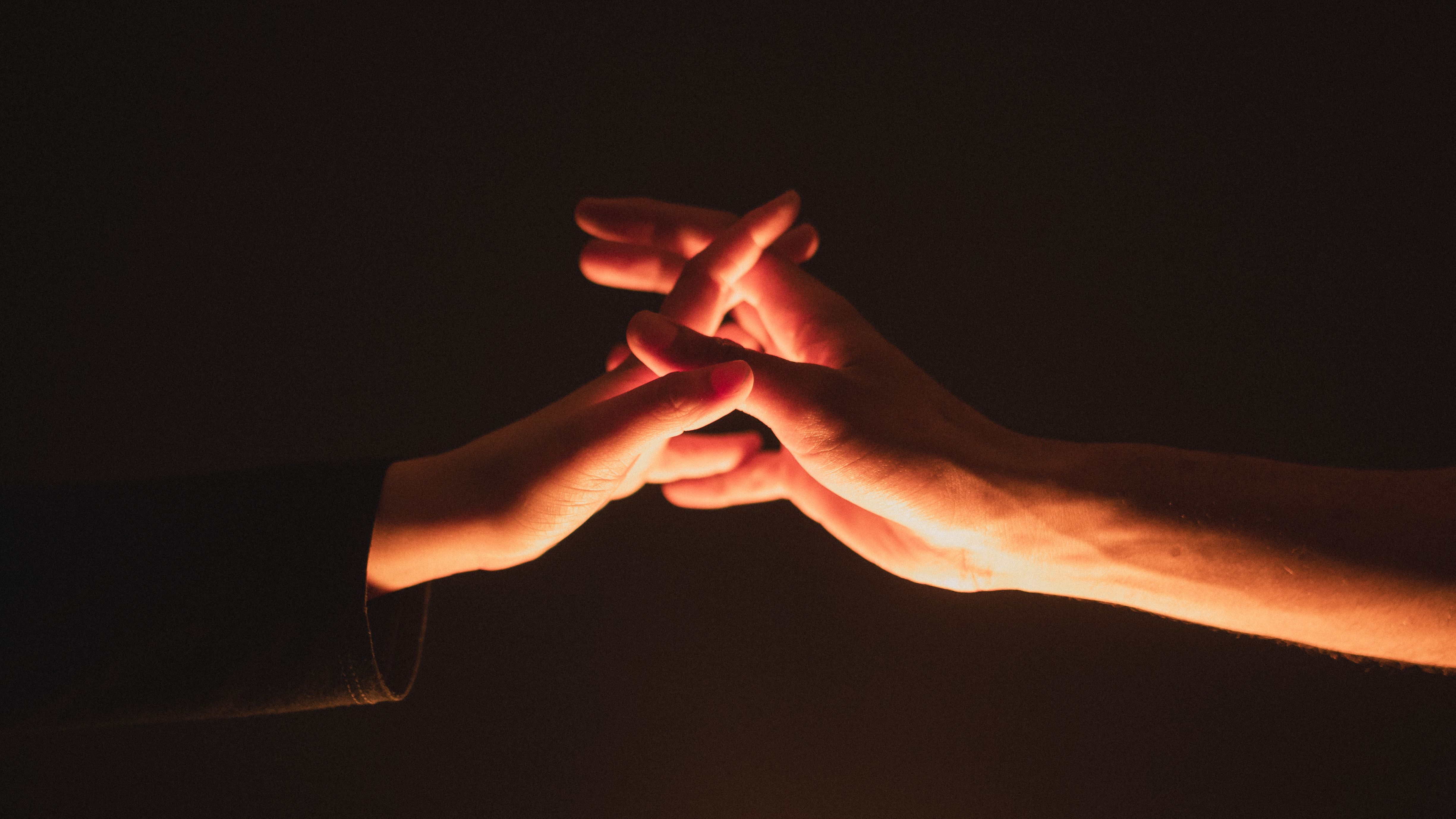 A close-up image showcasing two hands reaching towards each other in warm lighting.