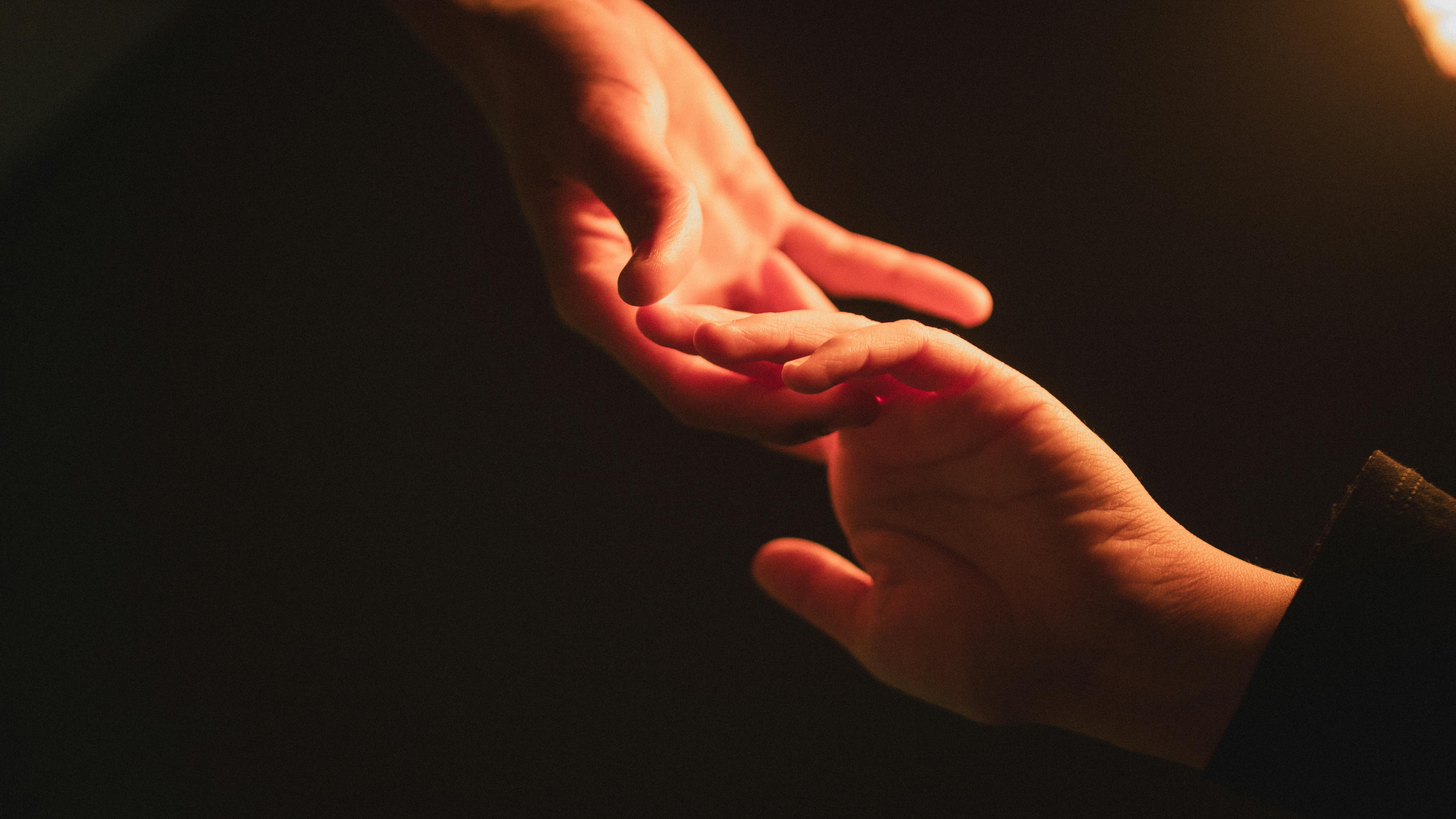 Intimate close-up of two hands reaching towards each other in warm light, symbolizing connection.