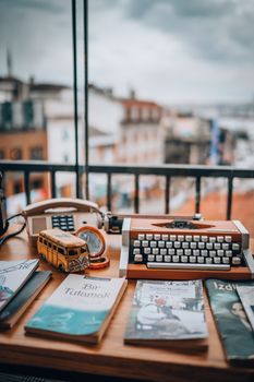 A cozy setup with a vintage typewriter, books, and a toy bus on a wooden table overlooking a cityscape.