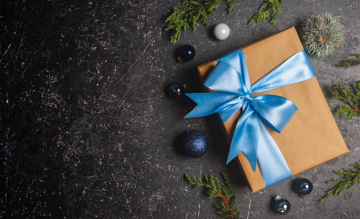 Gift box with blue ribbon and Christmas ornaments on a dark textured background.