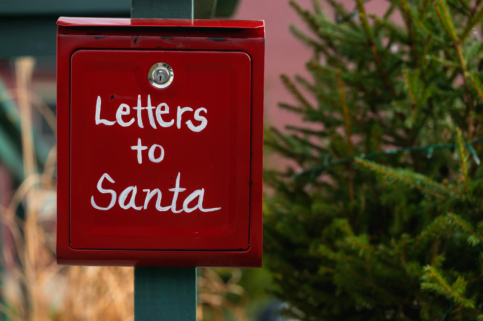 Red mailbox labeled 'Letters to Santa' amidst holiday greenery.