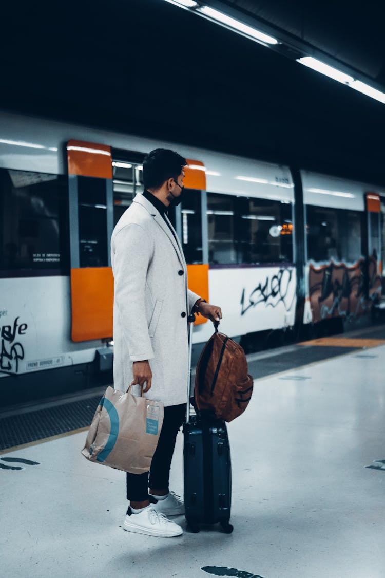 A Man In White Coat Standing While Holding His Luggage