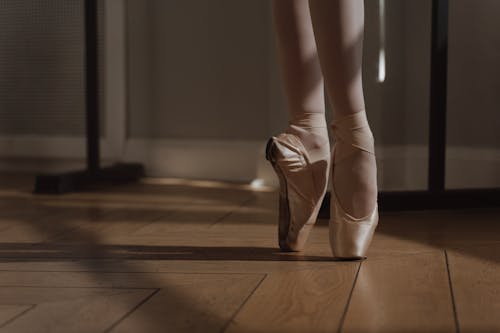 A Person Wearing Ballet Shoes on a Wooden Floor
